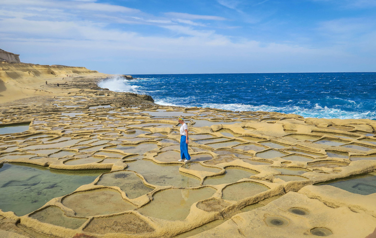 Frau läuft über die mit Meerwasser gefüllten Salzpfannen von Gozo