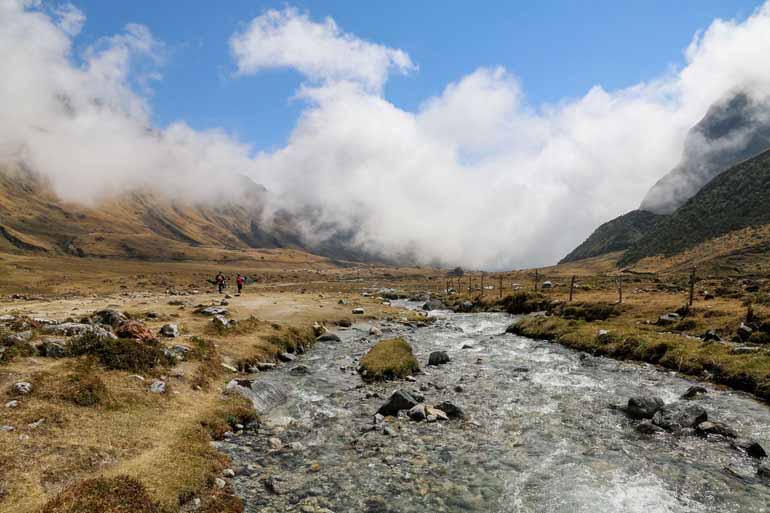 Bei einem Fluss, Nahe einem Bergtal sind zwei Wanderer auf ihrem Salkantay Trek in Peru unterwegs.