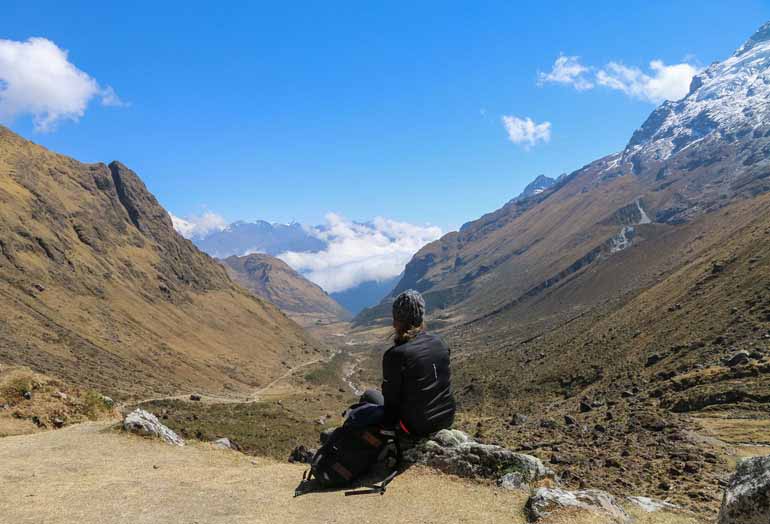 Die Bloggerin Manuela sitzt mit dem Rücken gekehrt zur Kamera und genießt die Aussicht auf die Berge während ihrer Wanderung zum Machu Picchu in Peru.