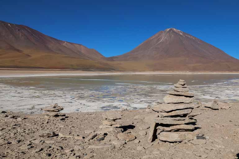 A stone slab tower with a lagoon and mountain in the background can be admired on a lagoon tour in Bolivia.