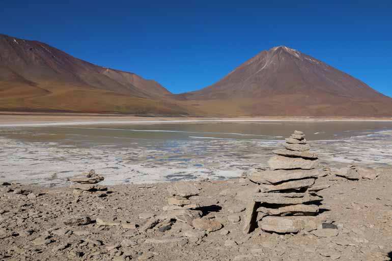 Ein Steinplattenturm mit Lagune und Berg im Hintergrund kann man bei einer Lagunentour in Bolivien bestaunen.