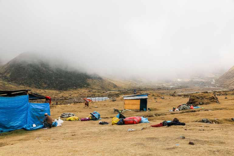 Ein Lagerplatz auf dem Weg zum Machu Picchu mit kleinen Hütten und Zelten im Nebel, im Hintergrund sind Berge zu erkennen.