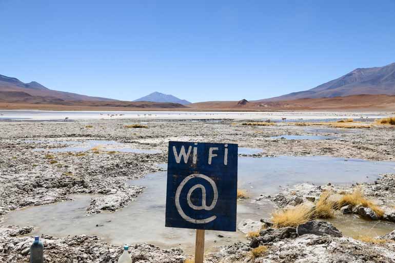 Mitten in der menschenleeren Laguna Hedionda in Boliven steht ein Schild mit der Beschriftung WiFi, in weiter Ferne sind Flamingos zu sehen.