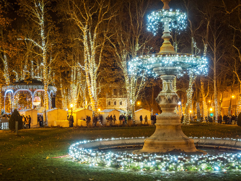 Auf dem Adventsmarkt in Zagreb ist ein Springbrunnen mit funkelndener Lichterkette geschmückt.