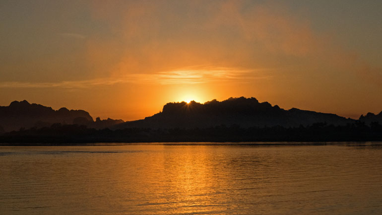 Rot-brauner Sonnenuntergang hinter den Bergen am Kan Thar Yar See bei Hpa An in Myanmar.