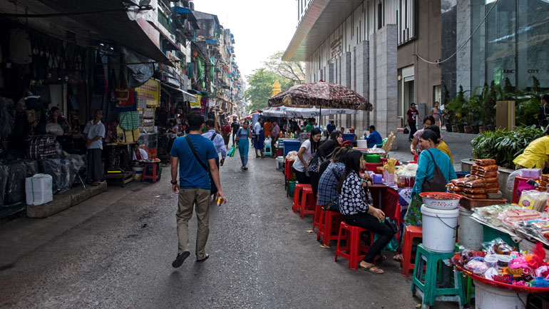 Myanmar: Passanten schlendern durch die Seitenstraßen von Yangon, vorbei an Essensständen.