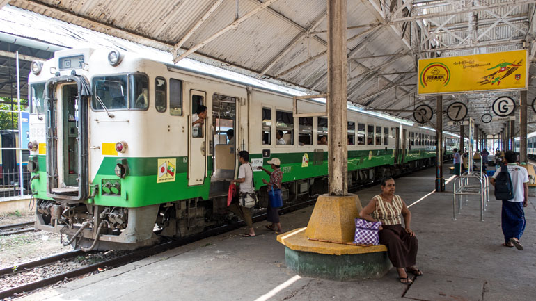 Am Bahnhof von Yangon in Myanmar steigen Passagiere in einen grün-weißer Zug ein.