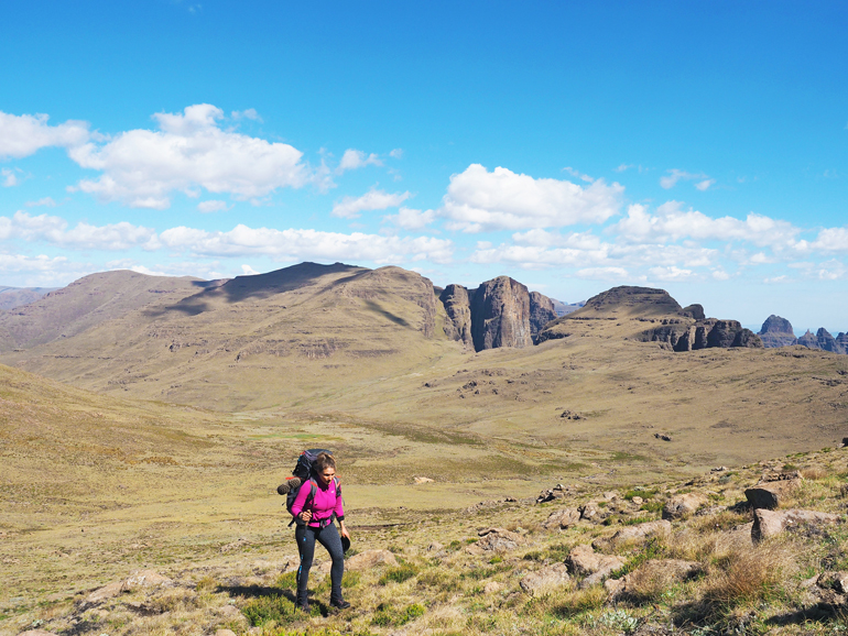 Südafrika Drakensberge: Eine Frau in einem Tal mit einem Rucksack auf dem Rücken.