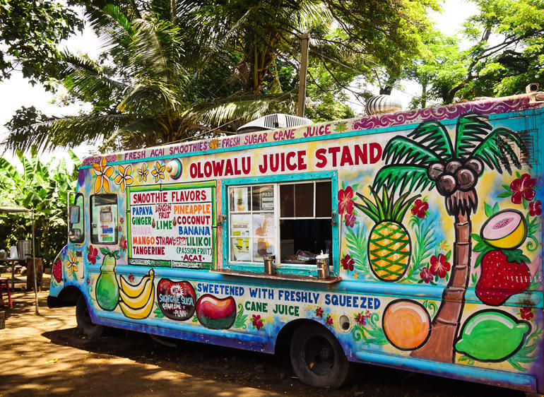Den bunt mit Früchten bemalten Foodtruck Olowalo Juice Stand findet man unter einer riesigen Palme am Kanaha Beach Park in Maui.