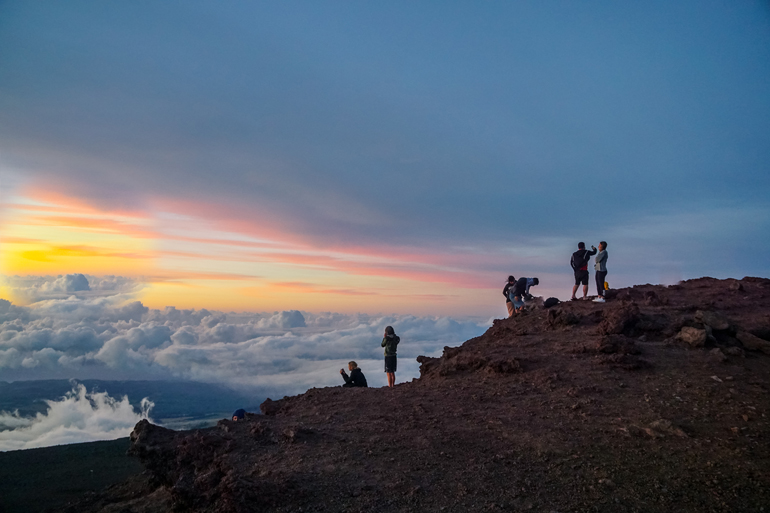 Auf dem Vulkan Mauna Kea auf der Insel Big Island genießen Besucher den Sonnenuntergang über den Wolken.