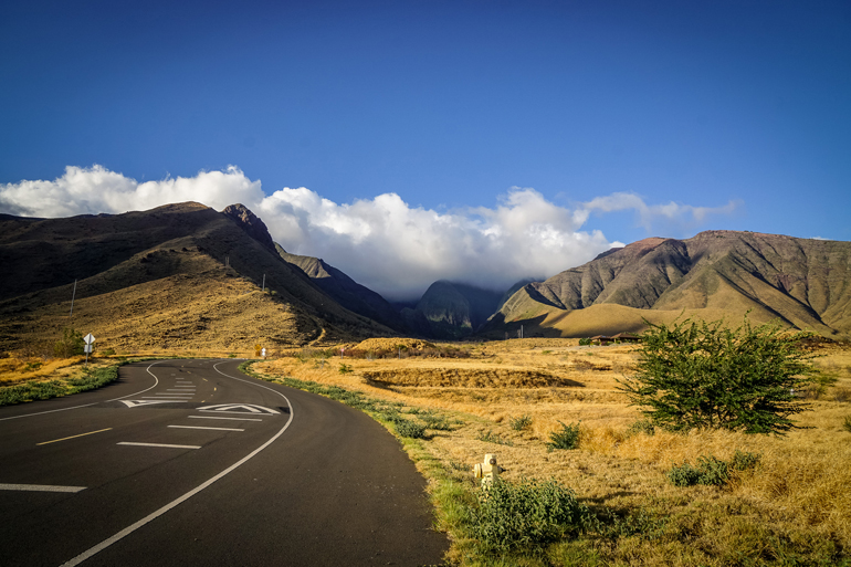The streets of Hawaii are fenced in by volcanic rocks behind which small clouds seem to be hiding.