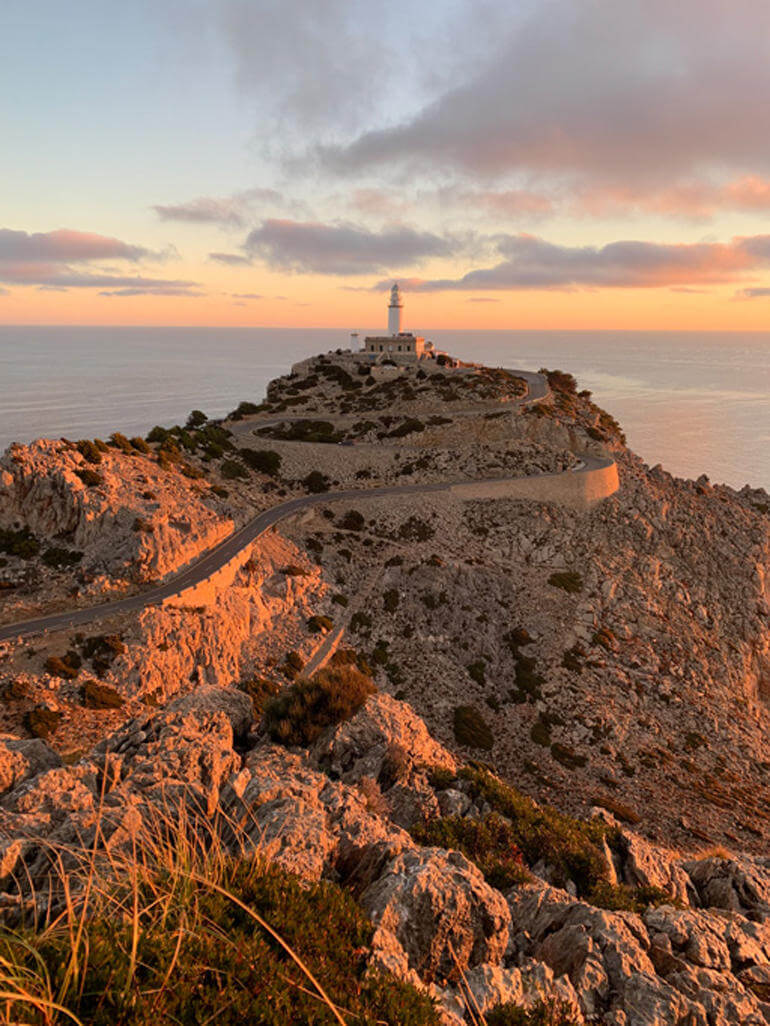 Beste Reisekamera: Ein Leuchtturm steht in der Ferne auf einem Berg, in der Abenddämmerung.