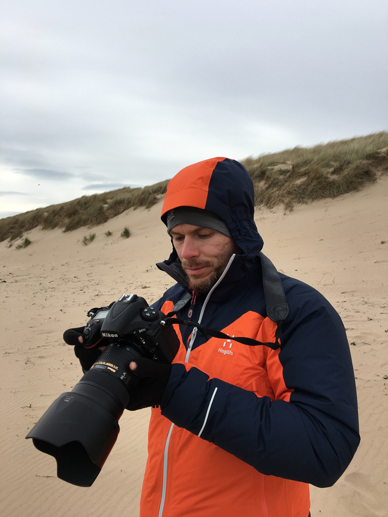 Beste Reisekamera: Ein Mann steht am Strand und hält eine Kamera in der Hand.