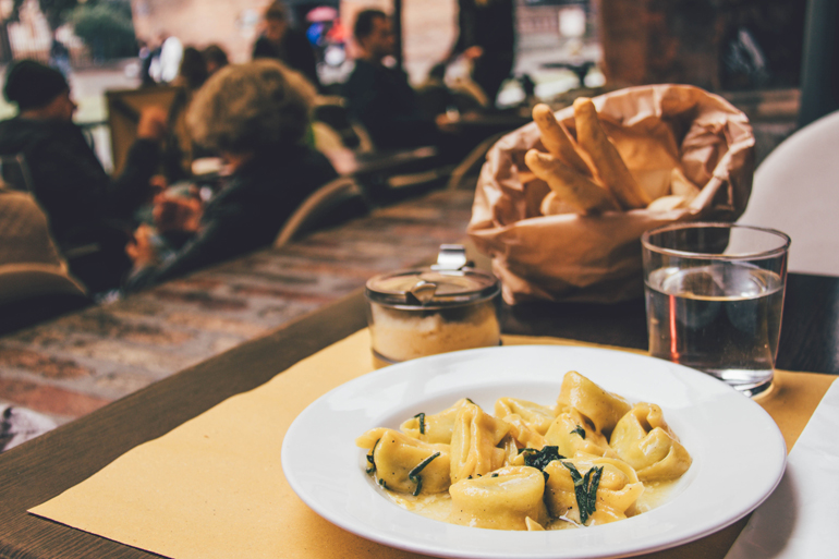 Tipp für Essen in Bologna: Ein angerichteter Teller mit Tortellini auf einem gedecktem Tisch.