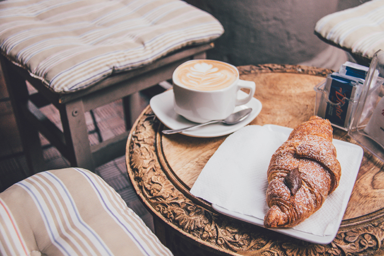Tipps für gutes Essen in Bologna: Auf einem Tisch steht ein Cappuccino und ein Croissant.
