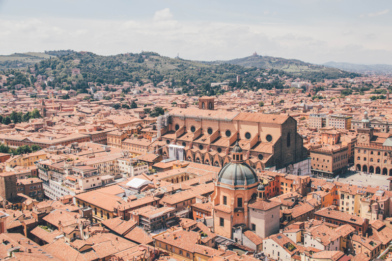 Bologna aus der Vogelperspektive: Ausblick auf orangene Dächer und grüne Berge im Hintergrund.
