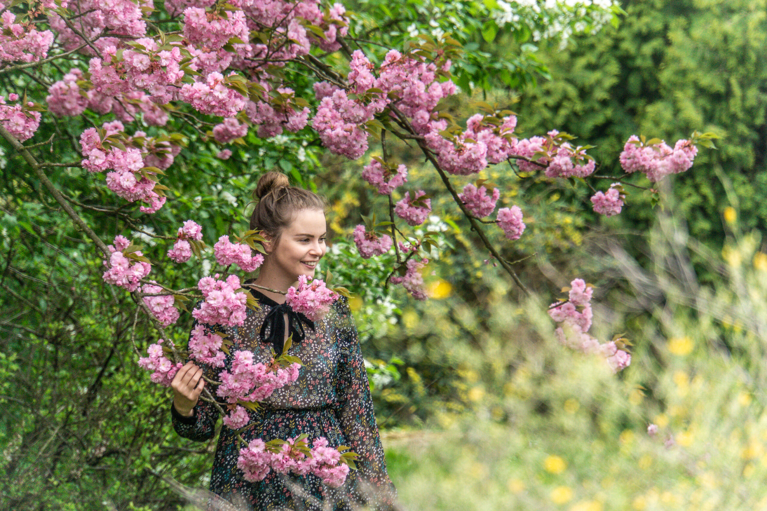 Eine Frau steht zwischen einem Baum an dem rosa Blumen hängen.