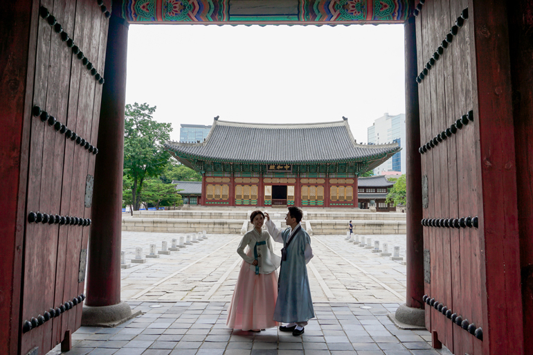Seoul Sehenswürdigkeiten: Ein Paar steht in traditioneller Kleidung in einem Tor, hinter ihnen befindet sich ein traditionelles Gebäude.