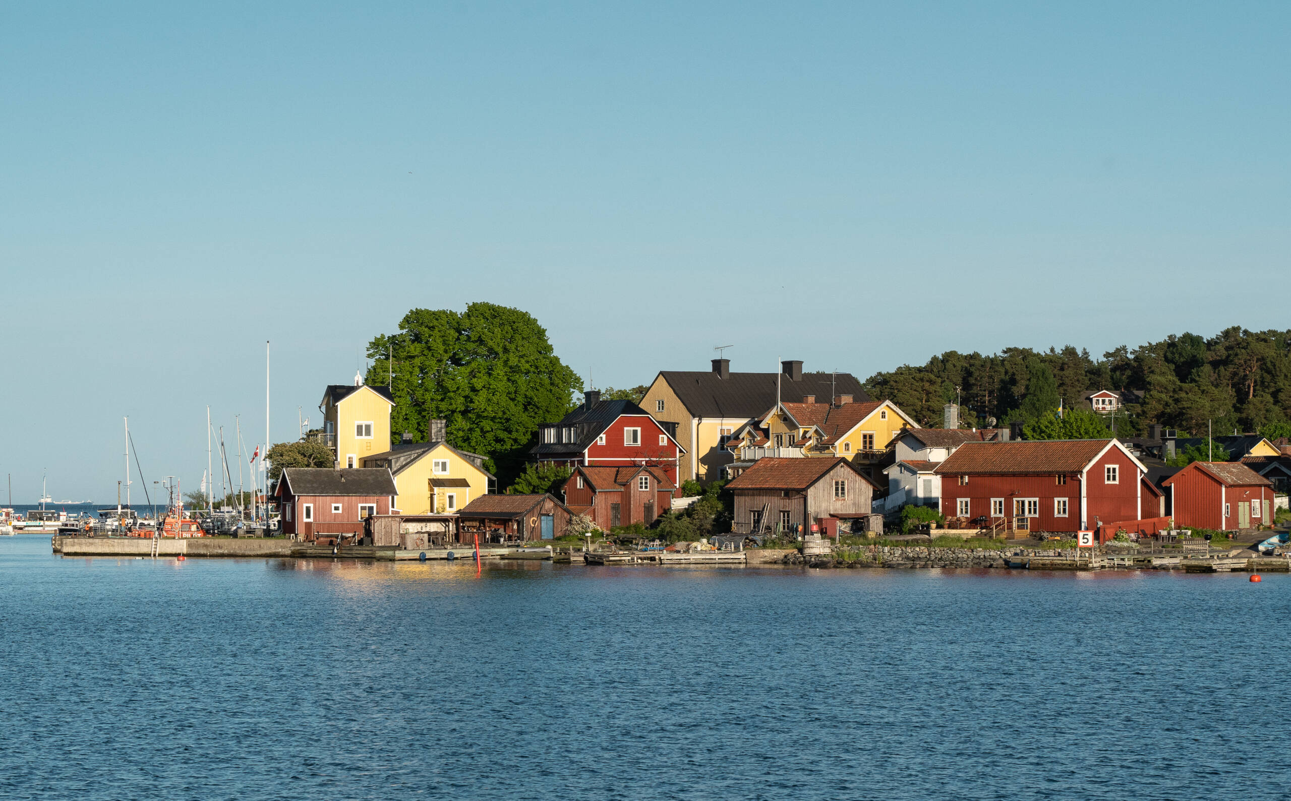 Ein kleines Dorf mit Holzhäusern in verschiedenen Farben und ein kleiner Hafen auf der Schäreninsel Sandhamn.