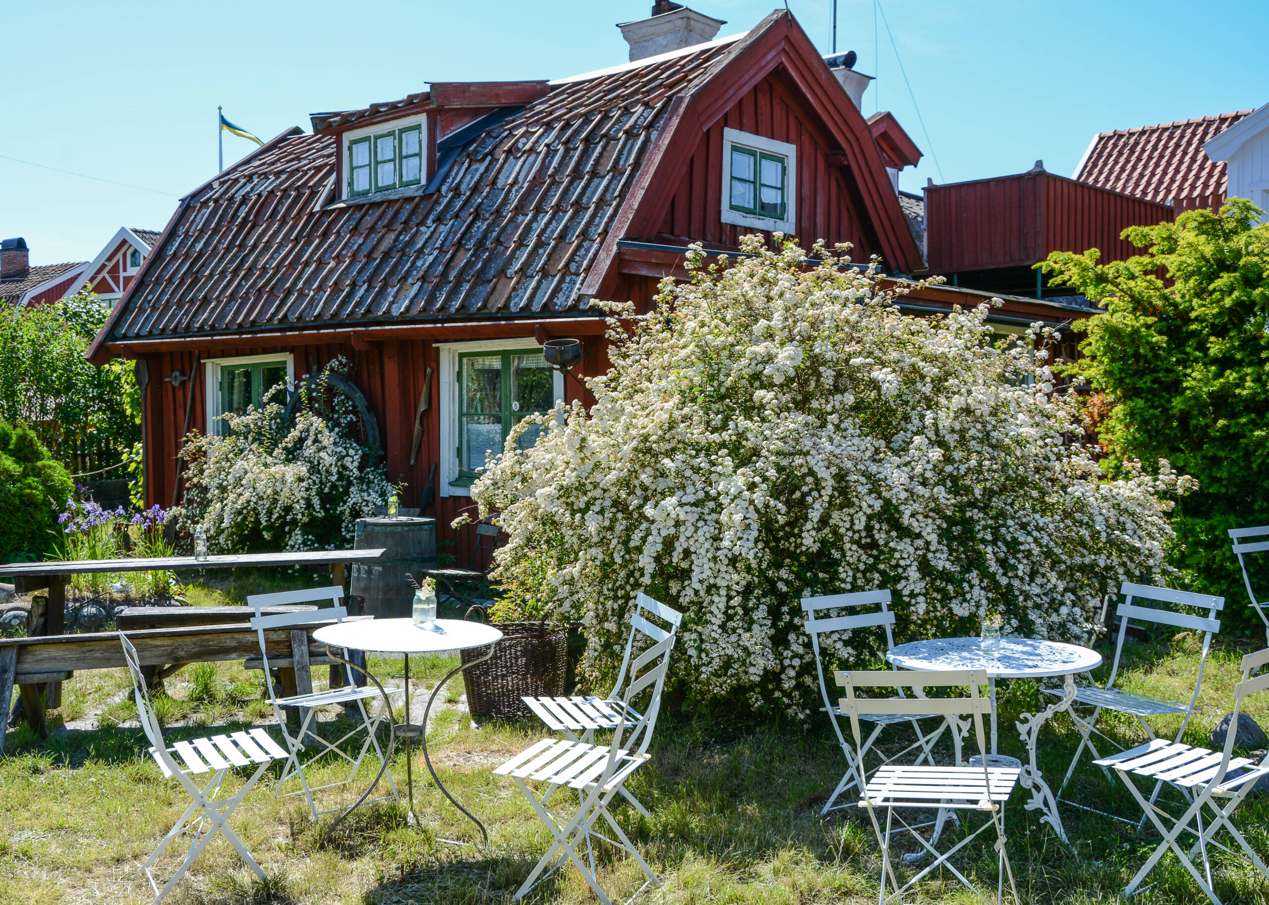 Das hübsche Gartencafé mit weißen Tischen und Stühlen inmitten blühender Sträucher im Garten ist ideal für eine Kaffeepause.