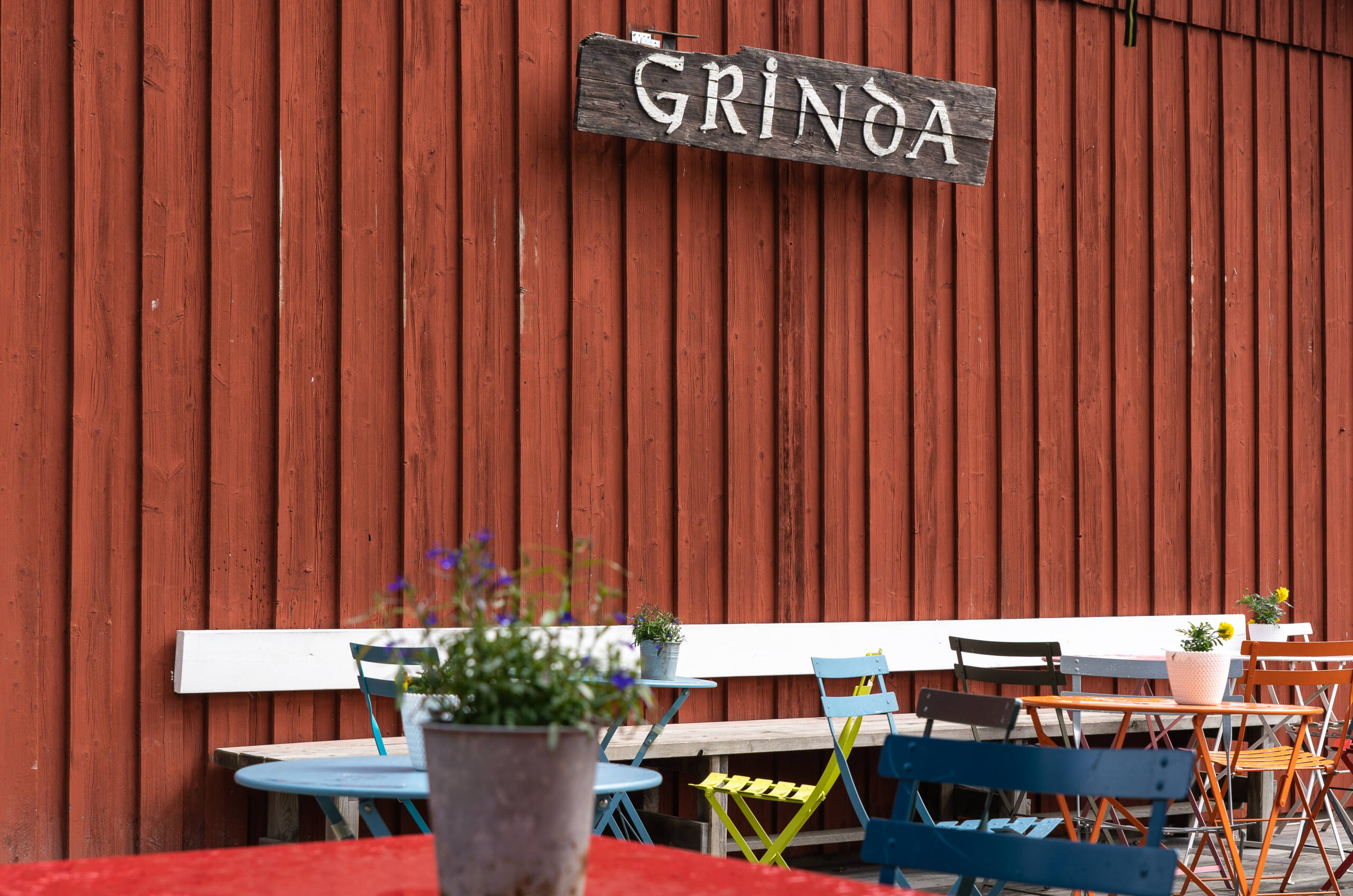 Bunte Stühle und Tische warten vor dem Grinda Lanthandel Café mit seiner roten Holzfassade auf Gäste.
