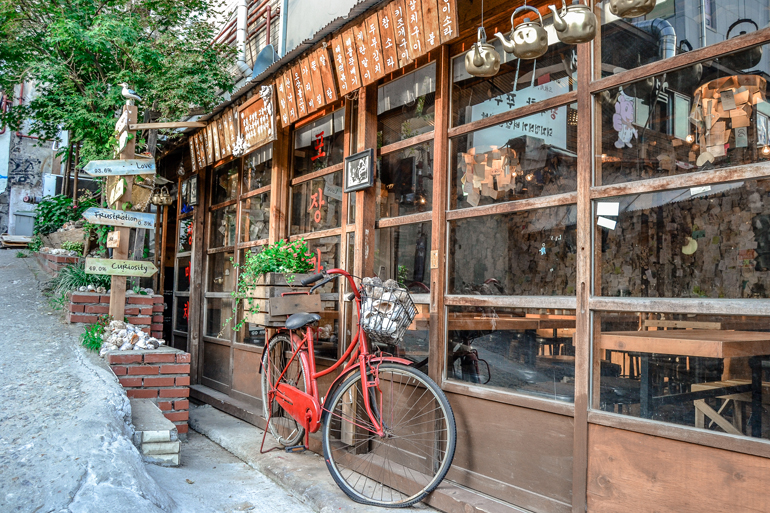 Seoul Sehenswürdigkeiten: In einem Holzhaus befindet sich ein Restaurant, davor lehnt ein rotes Fahrrad.