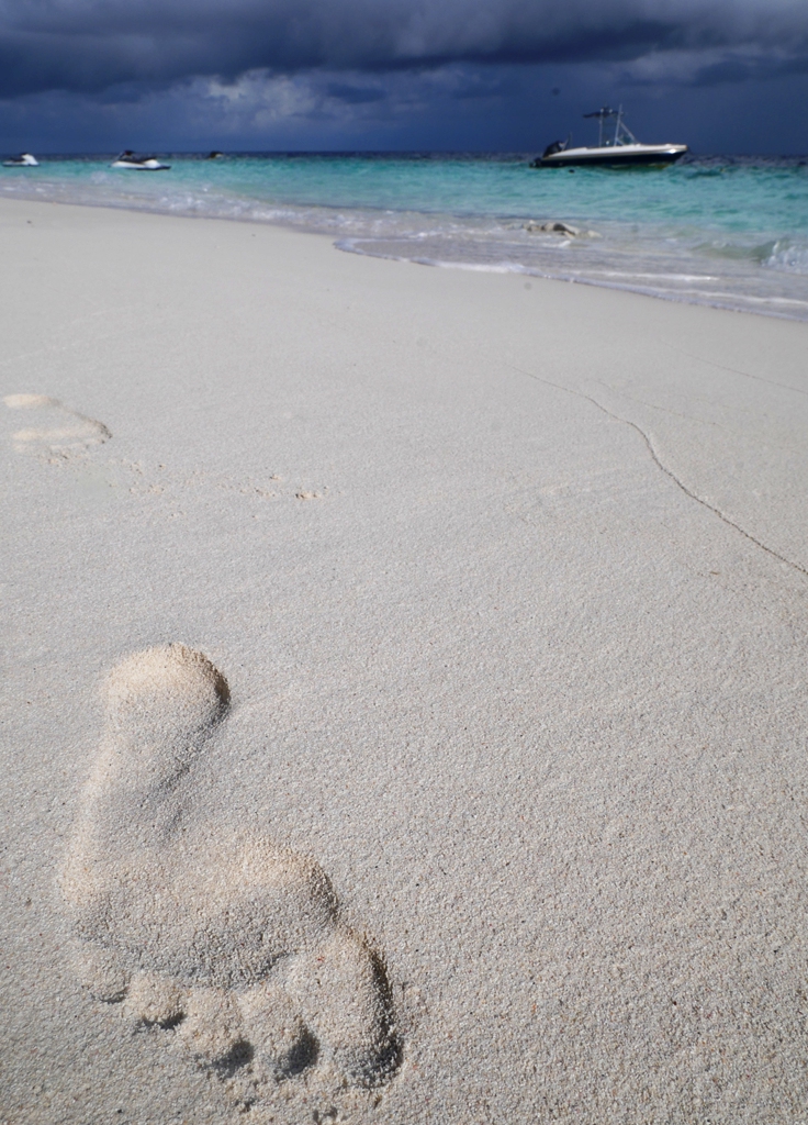 Ein einzelner Fußabdruck im Sand, dahinter das blaue Meer - beim allein Reisen lernt man viel über sich selbst.