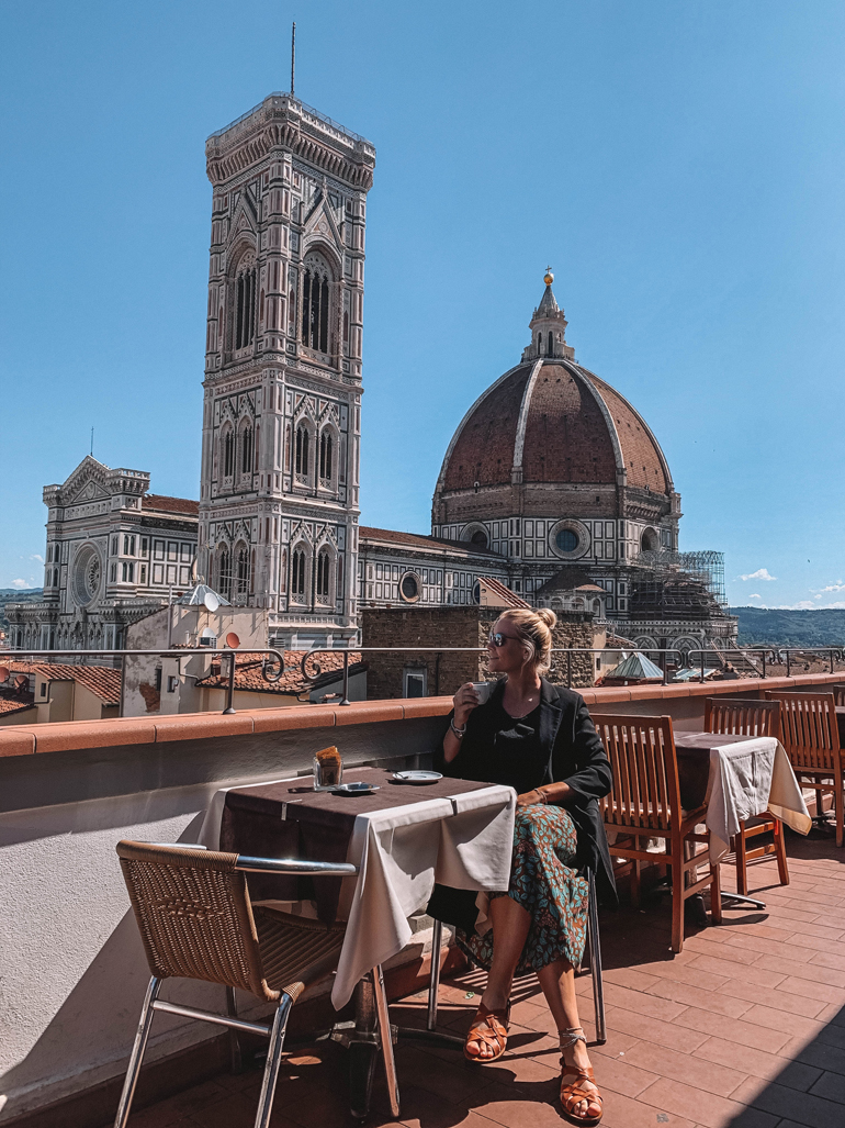 Florenz Geheimtipps: Eine Frau sitzt auf einer Dachterrasse, im Hintergrund eine Kirche.
