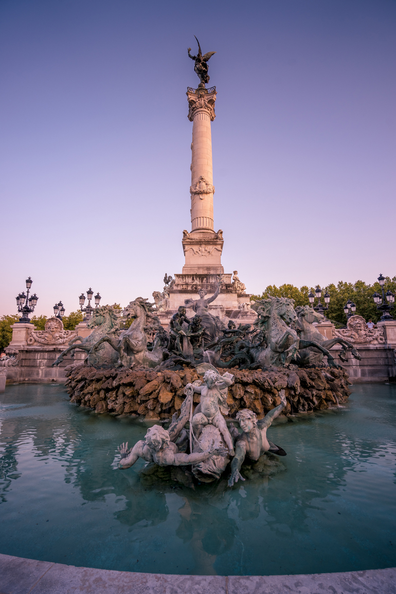 Städtetrip: Ein Brunnen mit einem kleinem Turm in der Mitte, an dem Skulpturen stehen.