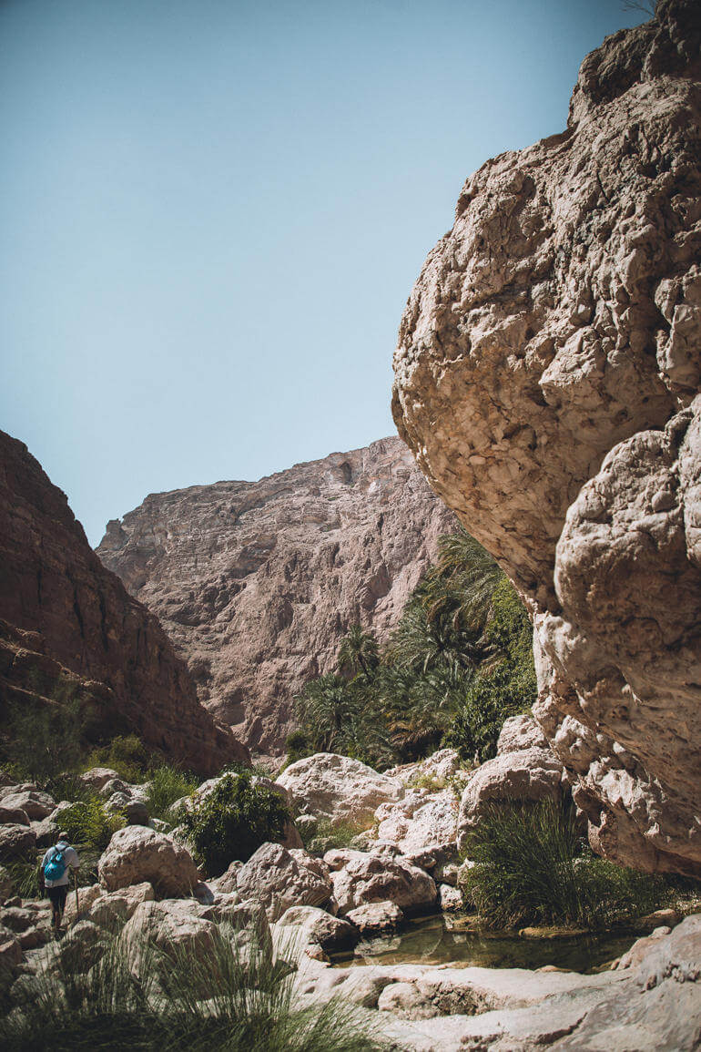 Ein Wanderer bahnt sich mit Gehstöcken den Weg durch Felsformationen der Wadi Shab im Oman.