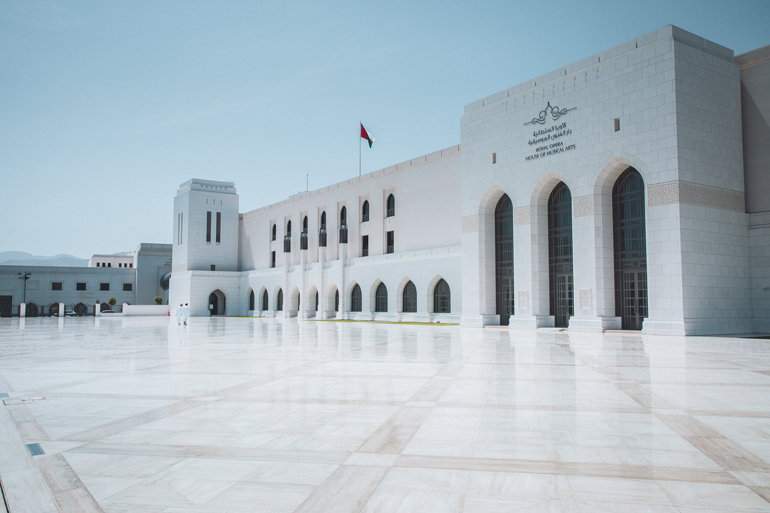 Das sehenswerte Royal Opera House mit seinen vielen Torbögen und Säulen in Maskat, Oman ist von einem riesigen Vorplatz mit großen weißen glänzenden Pflastersteinen ausgestattet.