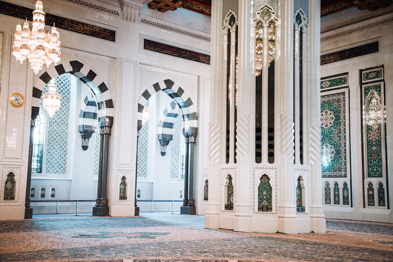 Im Inneren der Sultan-Qabus-Moschee in der Nähe von Maskat, Oman befindet sich an den hohen weißen Säulen und Torbögen feine Mosaike, und ein riesiger Gebetsteppich.