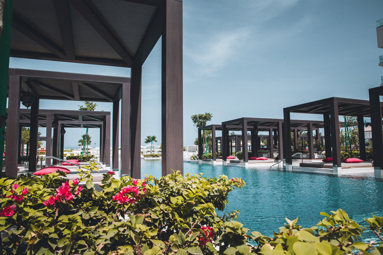 Ein breiter Pool-Fluss zieht sich im Hotel W Muscat im Oman durch die begrünte Anlage vorbei an überdachten hölzernen Liegeinseln.