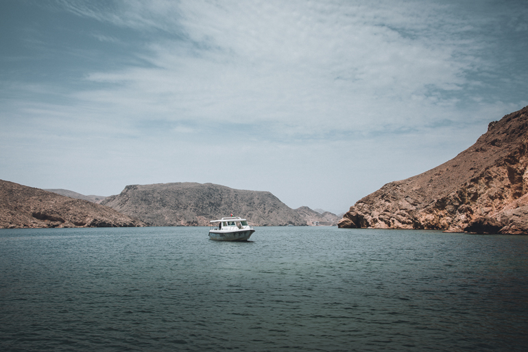 An der Küste von Omans Hafen Marina Bandar Al Rawdha schippert ein einzelnes Boot zwischen den Felsklippen.