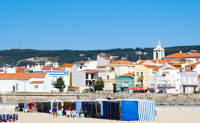 Am Strand von Buarcos in Portugal sitzen Menschen, dahinter erheben sich bunte Häuser.