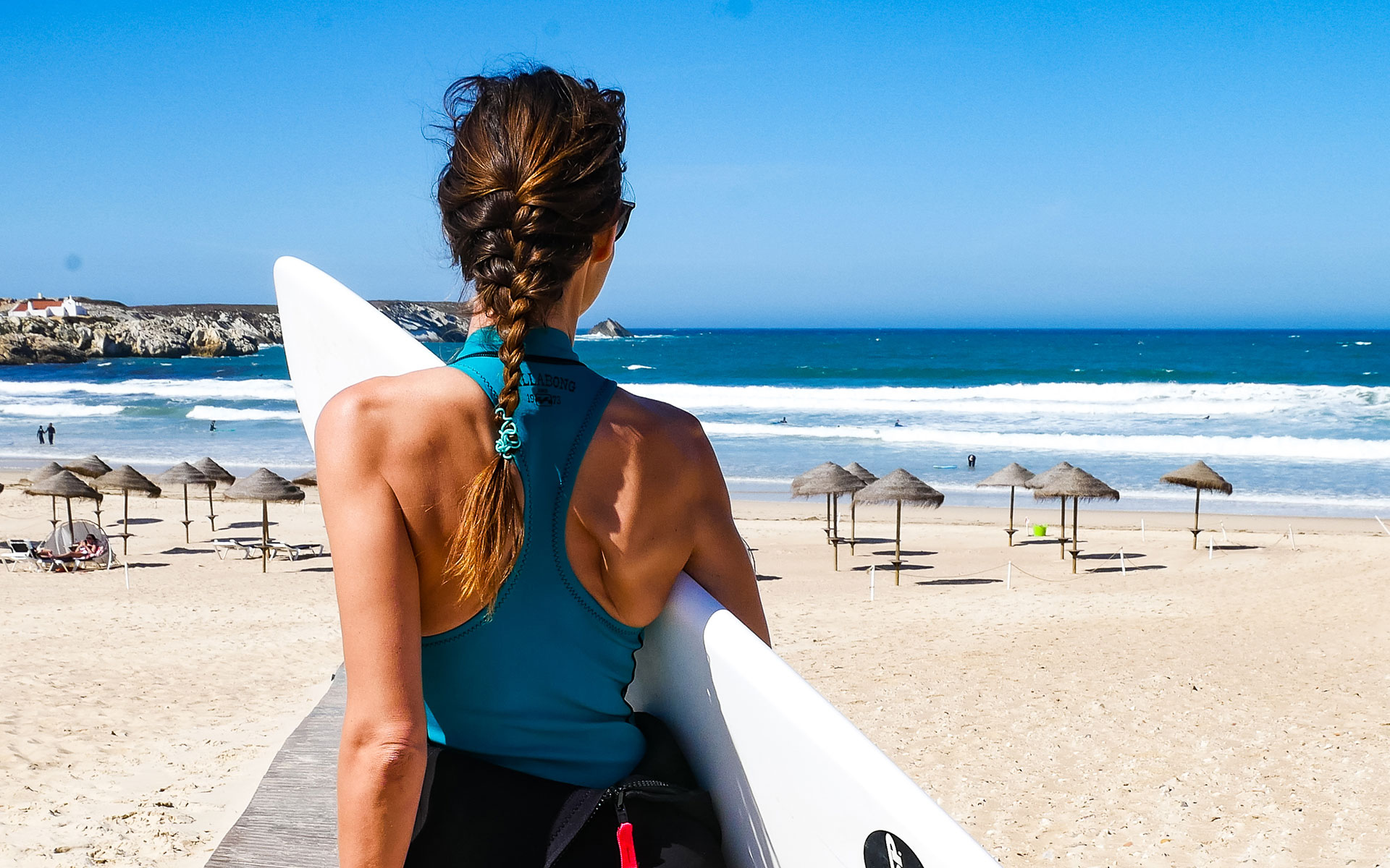 Bloggerin Anja Knorr mit dem Surfbrett unter dem Arm auf dem Weg zum Strand von Peniche in Portugal, wo hohe Wellen auf sie warten.