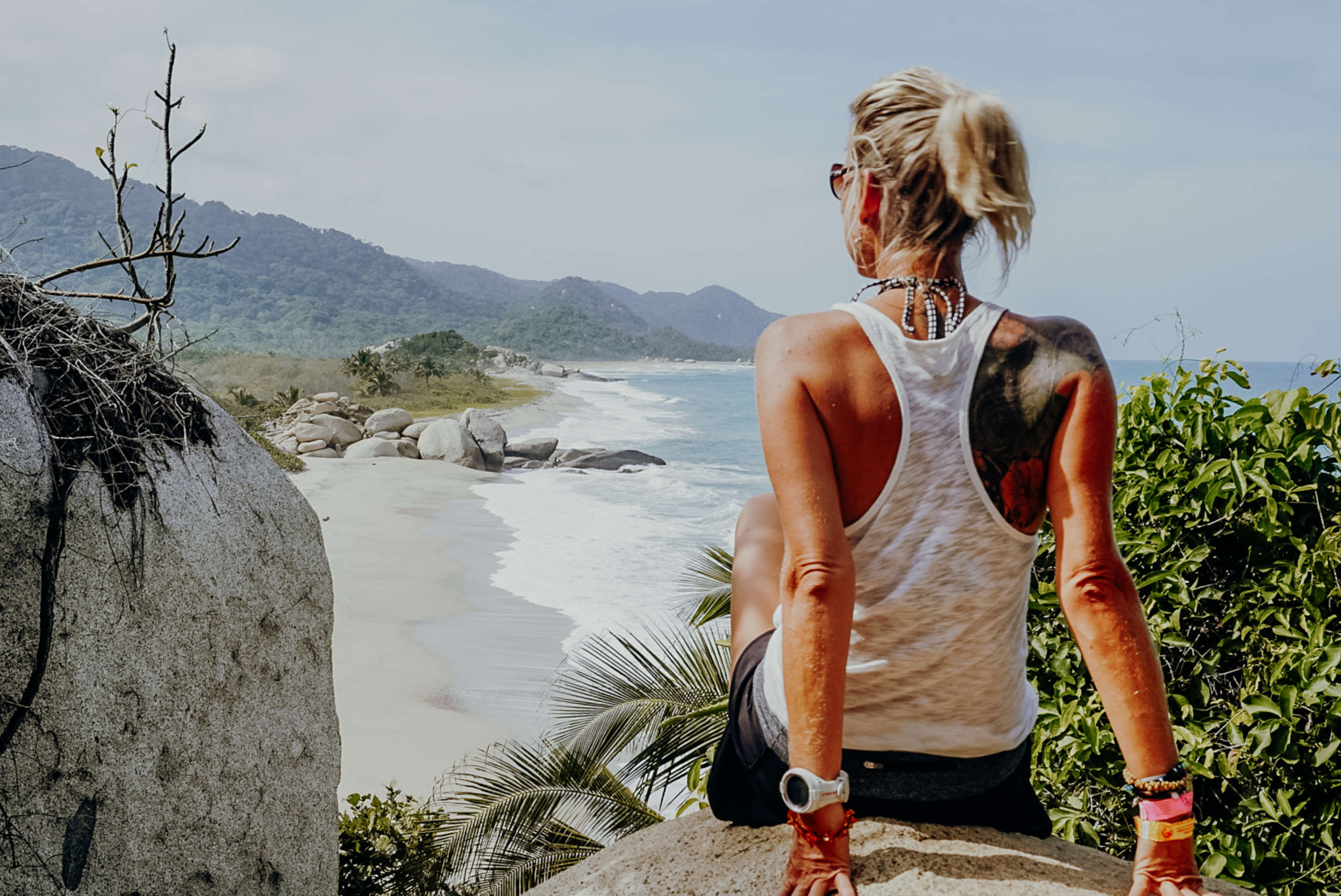 Paradisiacal beaches in the Parque Nacional Natural Tayrona. A woman sitting on a rock with the sea in the background.