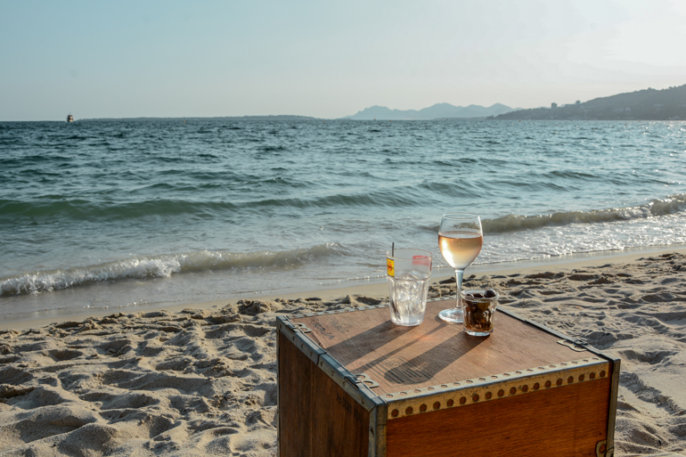 Ein kleiner Tisch der am Meer steht mit zwei Getränken drauf.