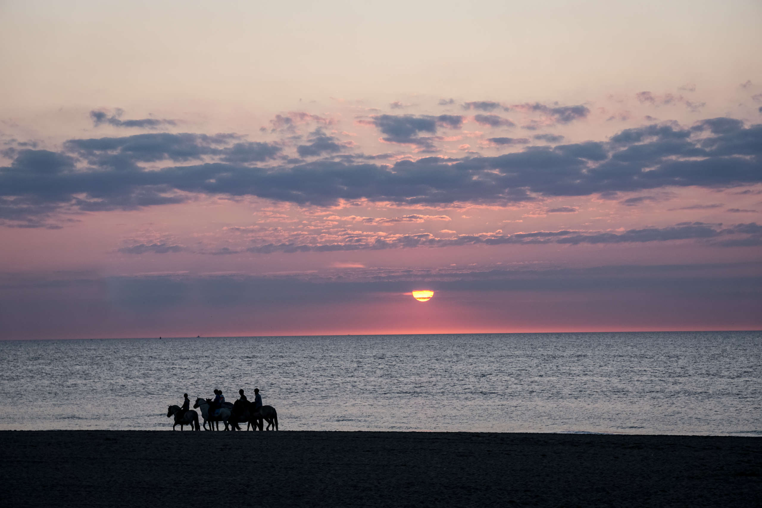 Sonnenuntergang am Meer, Reiter reiten den Strand entlang