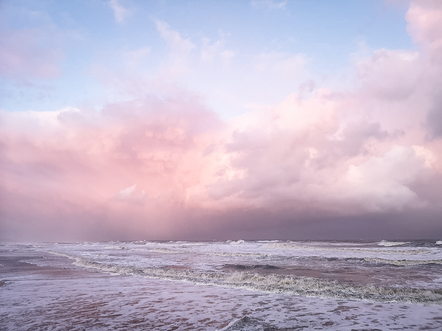 Die seichte Nordsee mit leichtem Wellengang, dahinter der sich pink färbende Himmel