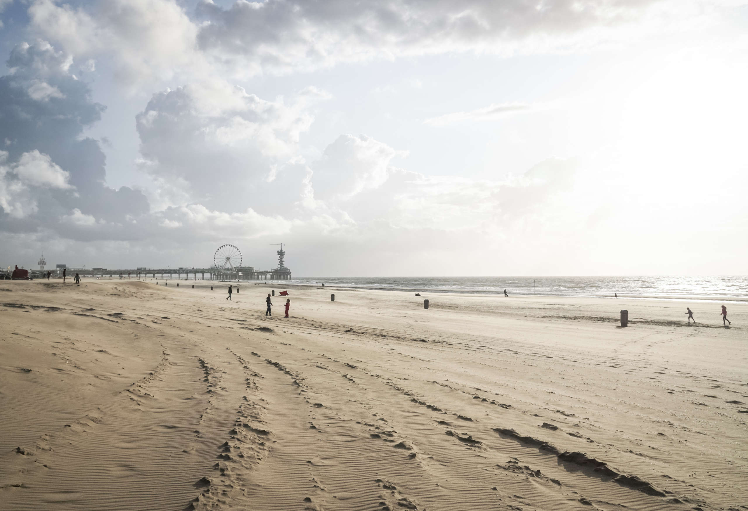 Ein weitläufiger Strand in Scheveningen an der niederländischen Küste, in der Ferne befindet sich ein Pier mit einem Riesenrad.