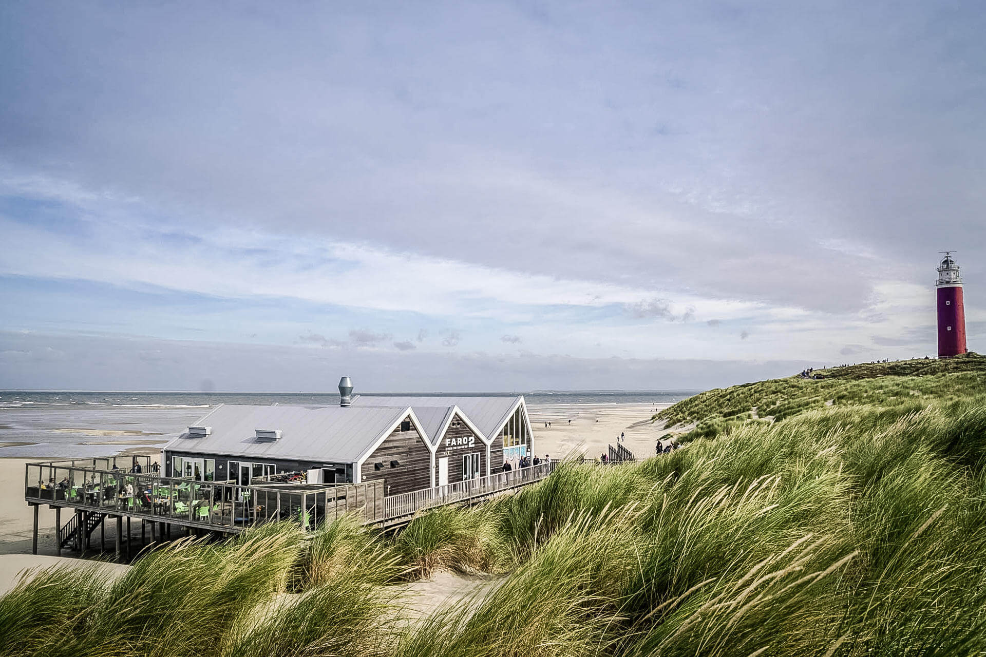 Blick auf Sandstrand und Meer in den Niederlanden, in der Ferne ein Leuchtturm und ein Fischerhaus
