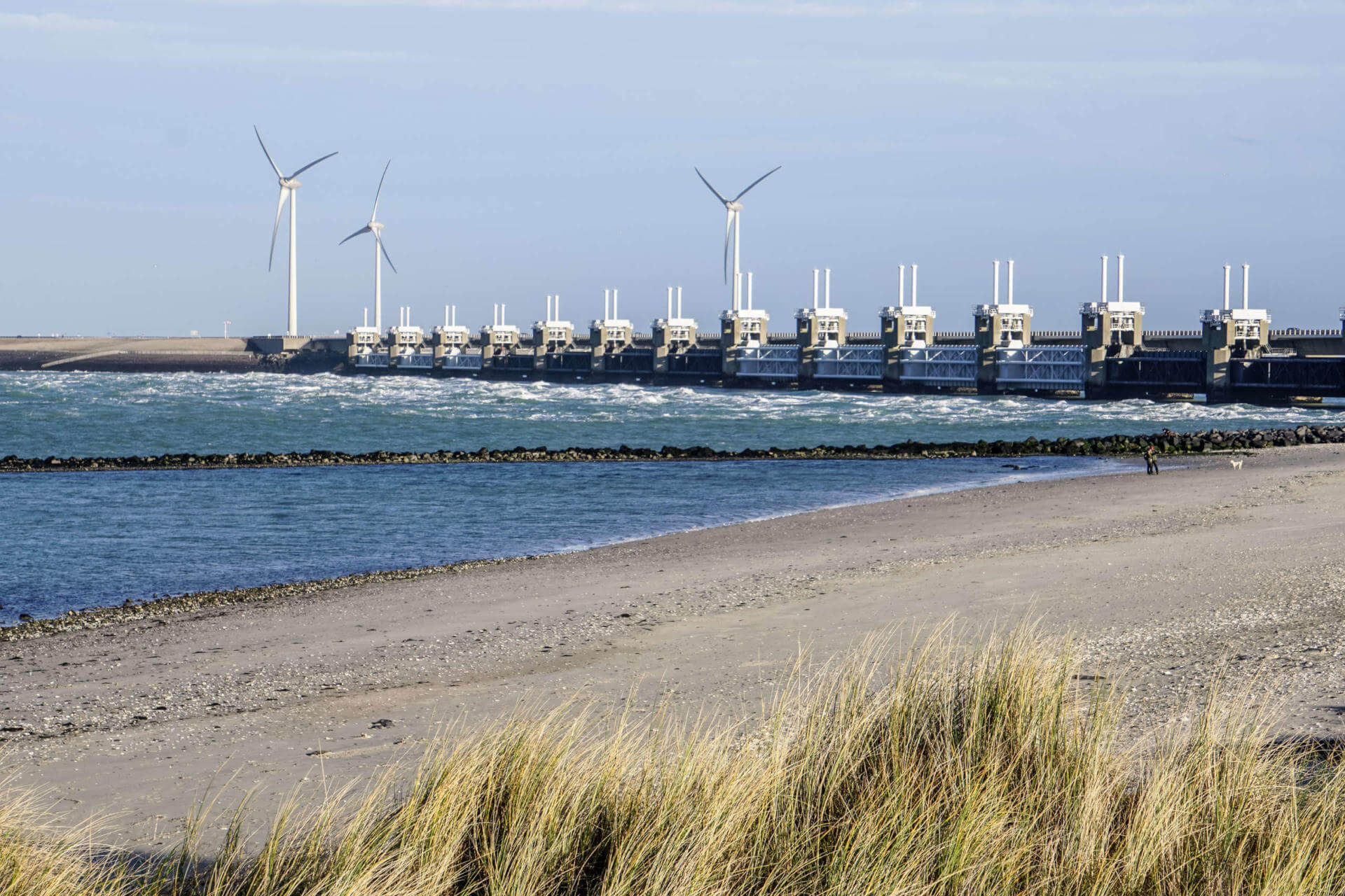 Windräder an einer Küstenschutzanlage der Deltawerke in Zeeland, Niederlande, davor das Meer und Strand