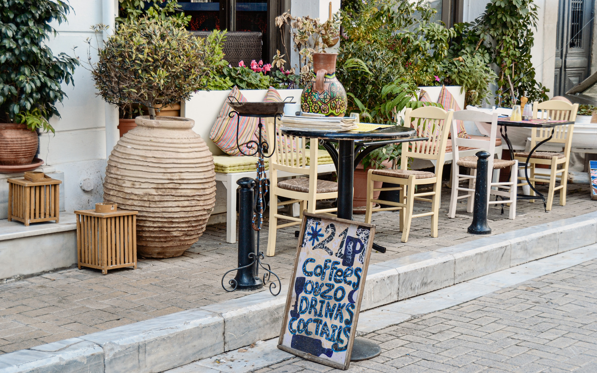 Athens kulinarische Seite erkunden: Außenterrasse eines Cafés im Stadtteil Plaka mit einladenden kleinen Stühlen und Tischen.