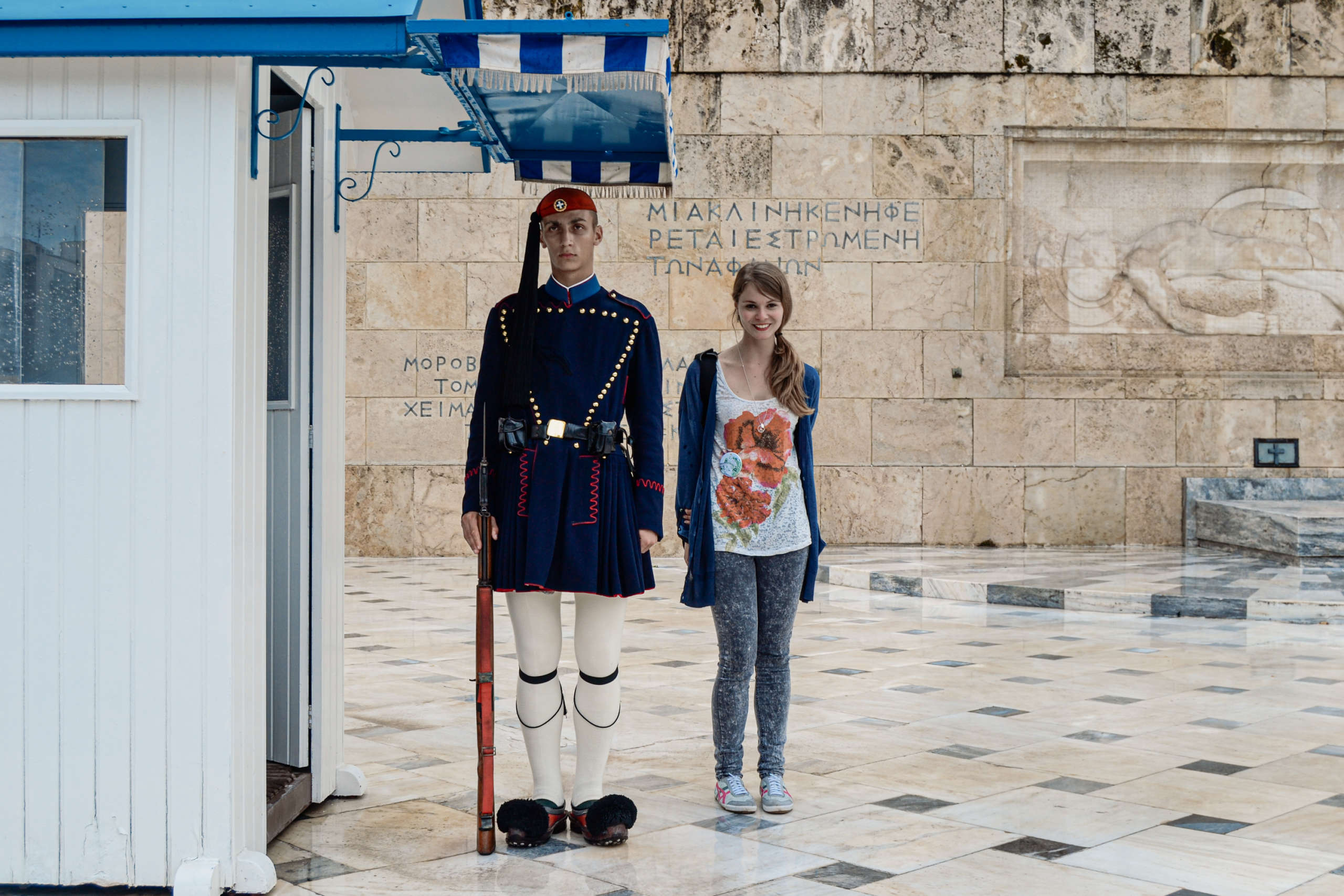 Ein Wächter im traditionellen Kostüm vor dem griechischen Parlament in Athen, neben ihm postiert eine lächelnde Frau für das Foto.