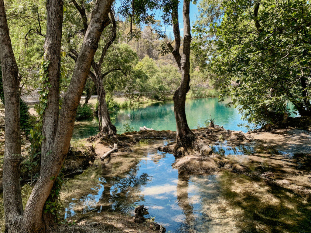 Geheimtipp Kroatien: Idyllische Wanderwege führen teils im Schatten unter Bäumen entlang der Krka Seen. Das Wasser schimmert türkisblau.