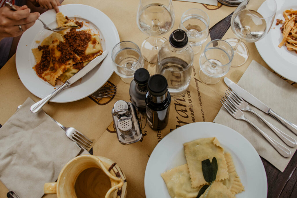 Ein gedeckter Tisch mit italienischen Pasta-Spezialitäten auf weißen Tellern, dazu gibt es italienischen Weißwein.