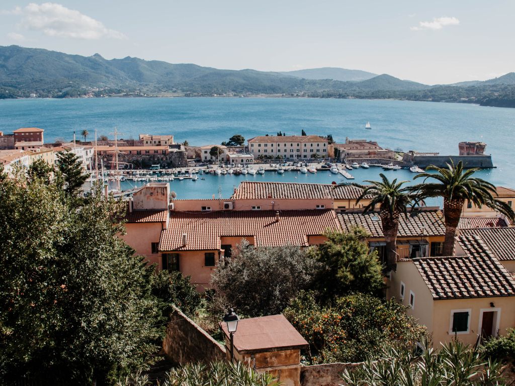 Von der Festung in Portoferraio aus haben Besucher der Insel Elba einen traumhaften Blick über Hausdächer und Palmen hinweg auf den sehenswerten Yachthafen. Im Hintergrund erheben sich die Berge der kleinen toskanischen Insel.