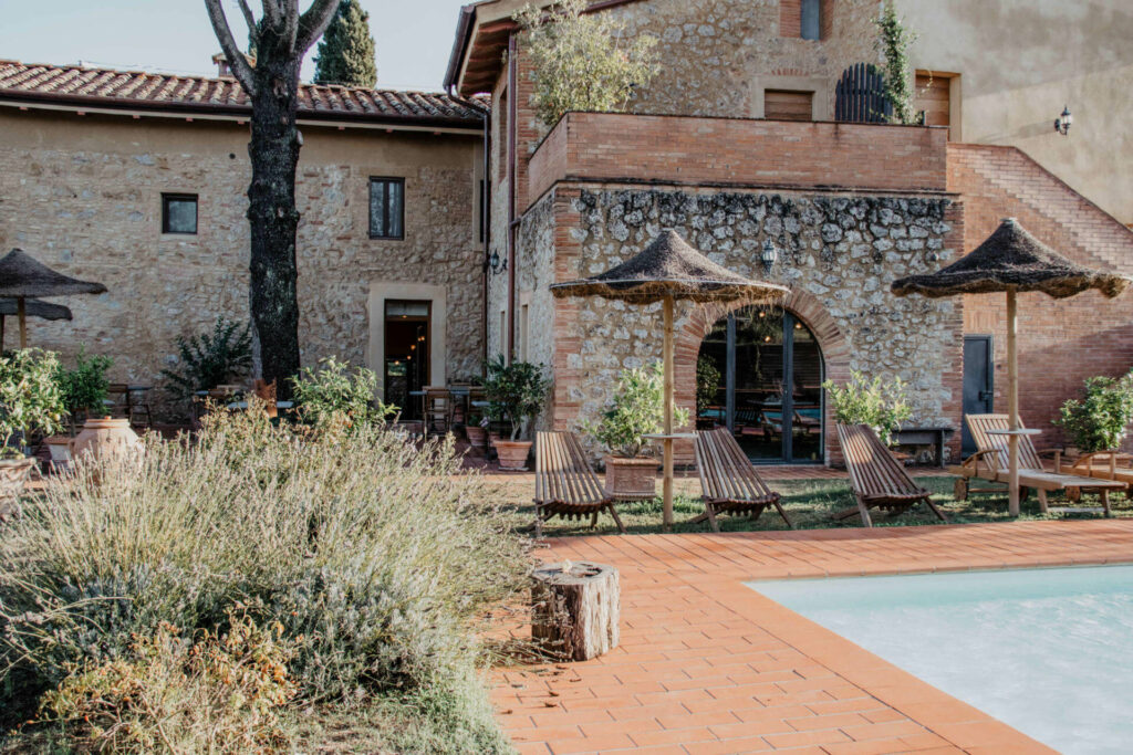 An dem von roten Pflastersteinen umrandeten Pool der Unterkunft Agrivilla i Pini im Herzen der Toskana stehen Liegestühle und Sonnenschirme für die Urlauber bereit.