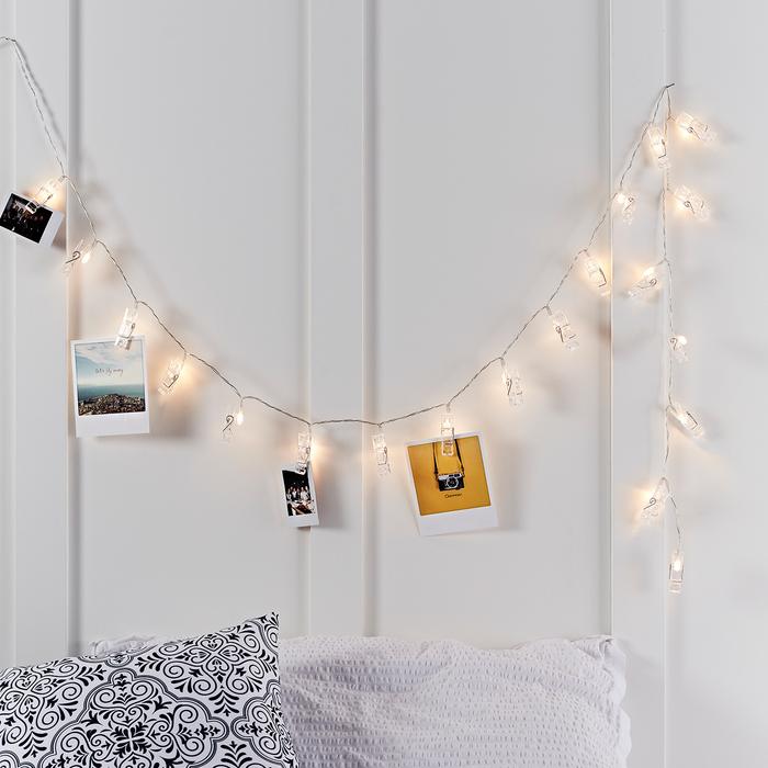 Ein dekoratives Geschenk für Reisefreunde: Bilder hängen an den Klammern einer mit LED-Leuchten ausgestatteten Lichterkette vor einer weißen Wand.